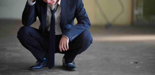 しゃがみこんで悩む男性の画像