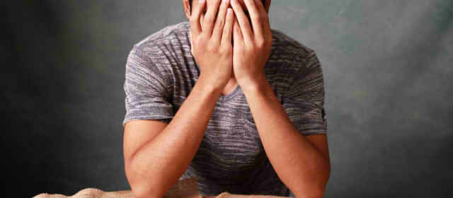 顔を覆って悩む男性の画像