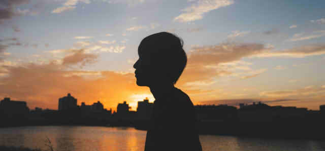 夕焼けをバックにたたずむ男性の画像