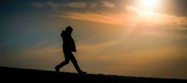 夕日をバックに歩く男性のシルエット画像