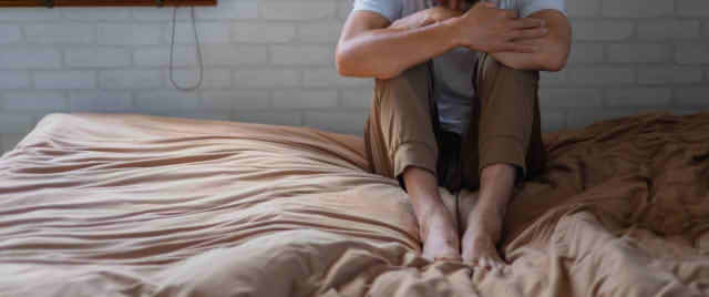 男性がベッドの上でうずくまる画像