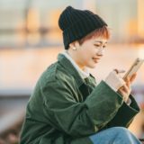 外でスマホを見て笑顔になる女性の画像