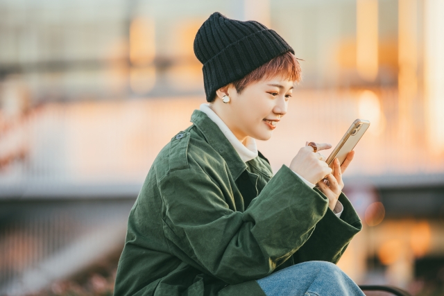 外でスマホを見て笑顔になる女性の画像