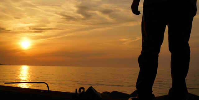 夕日をバックに海を眺める男性の後ろ姿の画像