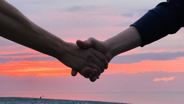 夕日をバックに男性二人が手をつなぐ画像