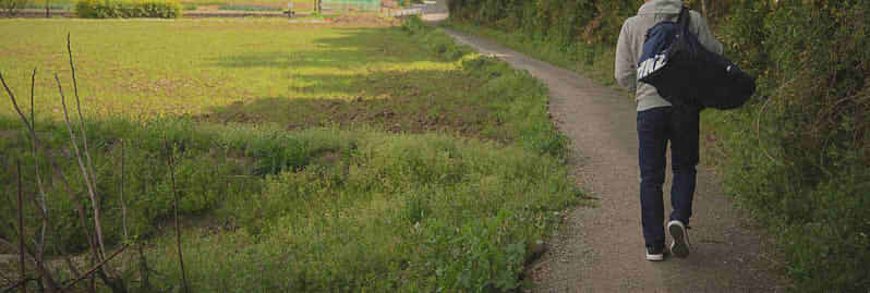 荷物を抱えて道を歩く男性の後ろ姿の画像