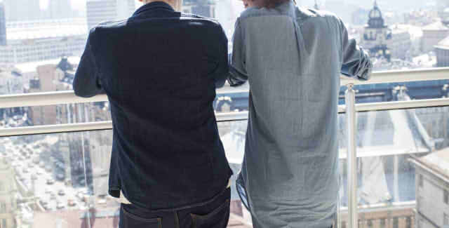 ベランダで肩を寄せ合う男性二人の後ろ姿の画像