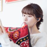 スマホを見ながらイヤホンで聴く女性の画像