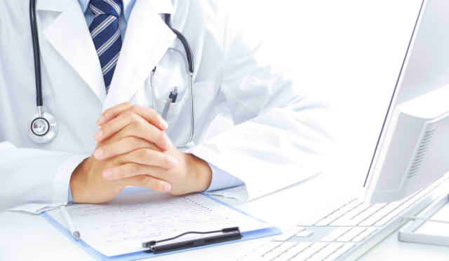 机の上で手を組む男性医師の画像