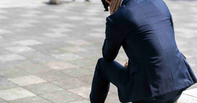 座り込んで俯くスーツの男性の画像