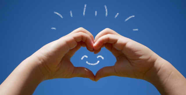 空をバックにハートのハンドサインの画像