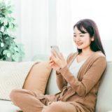 ソファーでリラックスしながらスマホを触る女性の画像