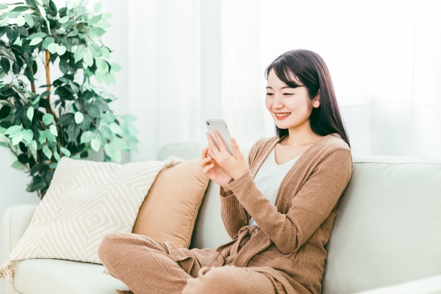 ソファーでリラックスしながらスマホを触る女性の画像